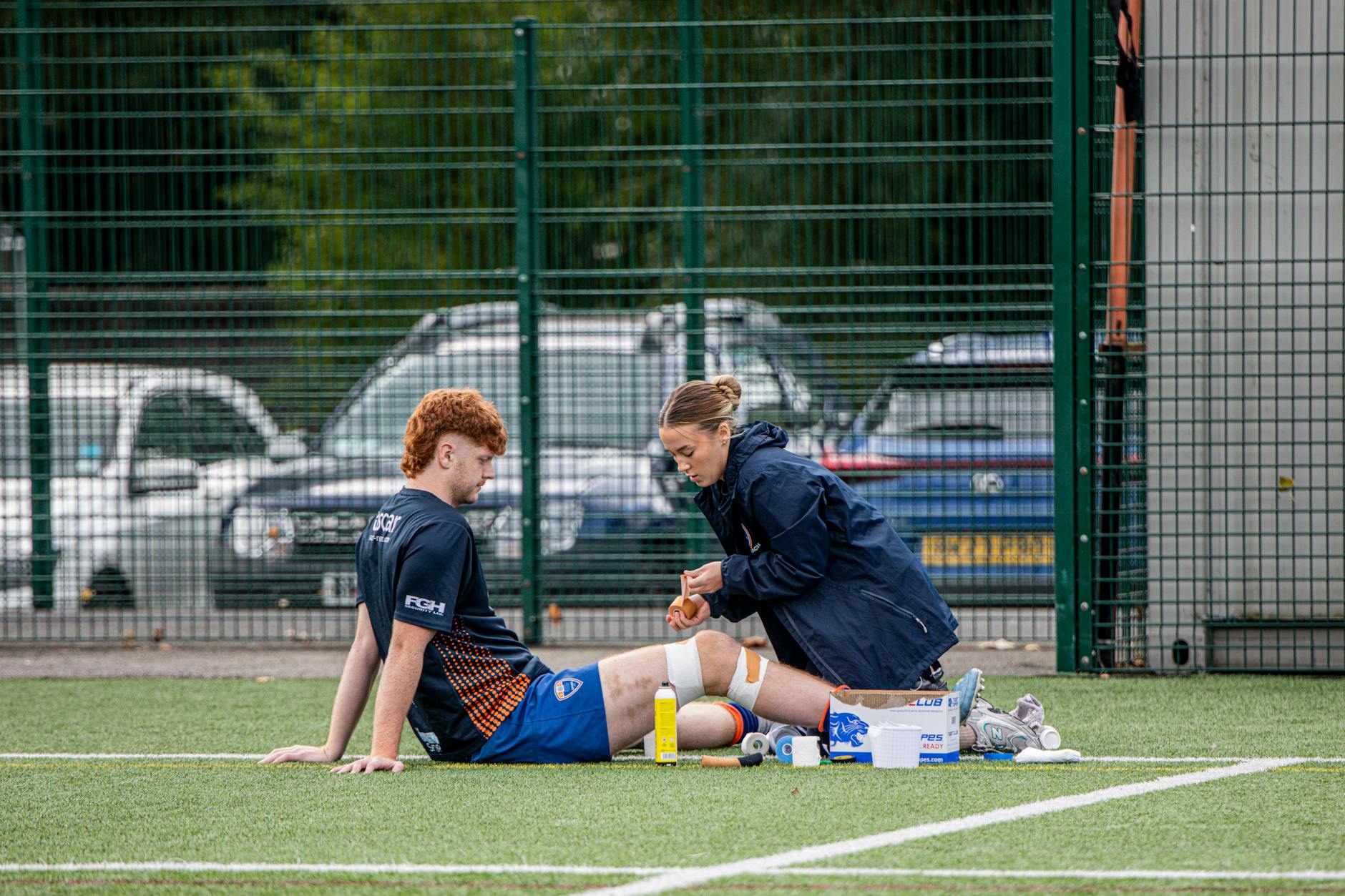 A sports therapist tends to an injured athlete on an outdoor football field.