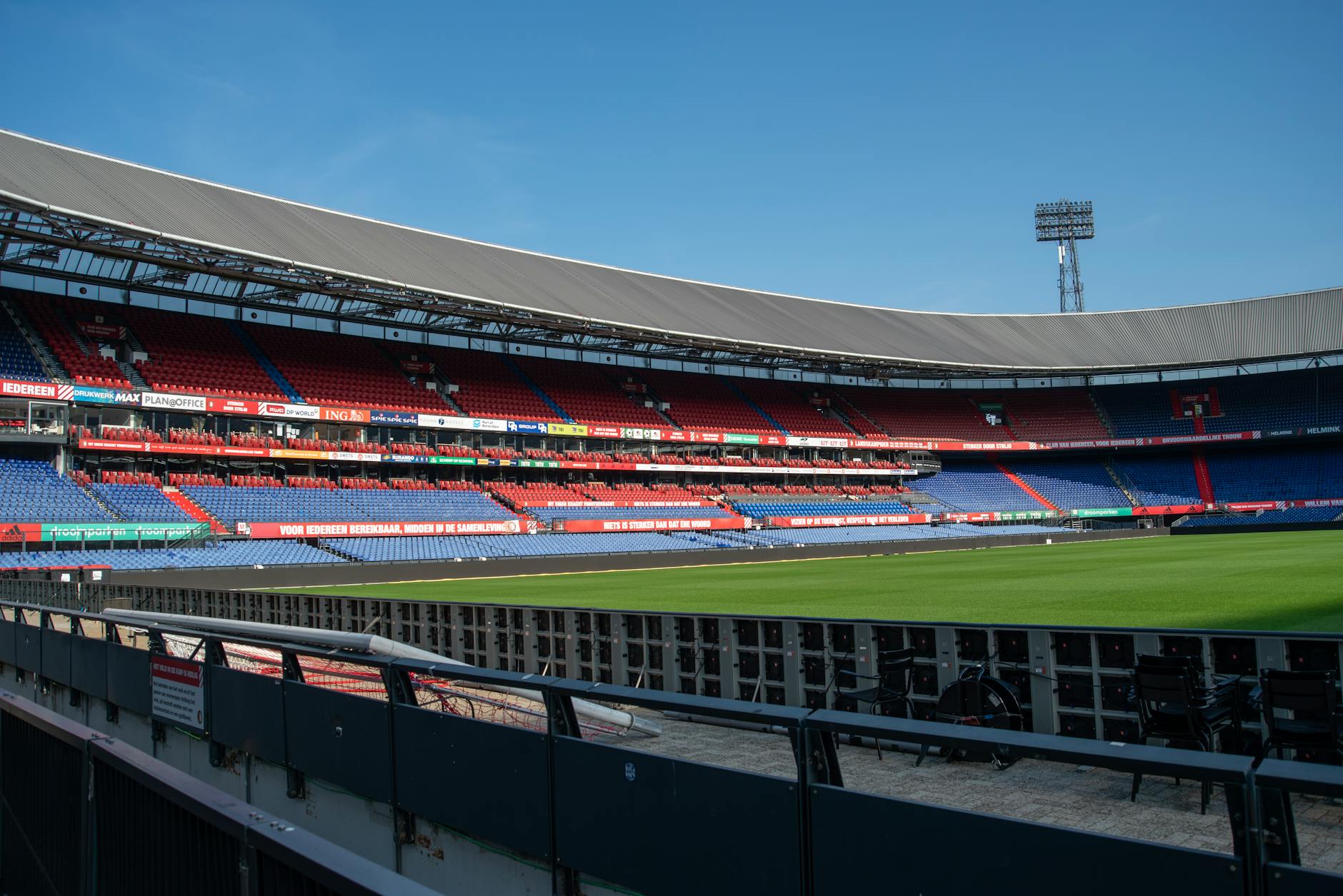Panoramic view of De Kuip stadium in Rotterdam with empty stands and a clear blue sky.