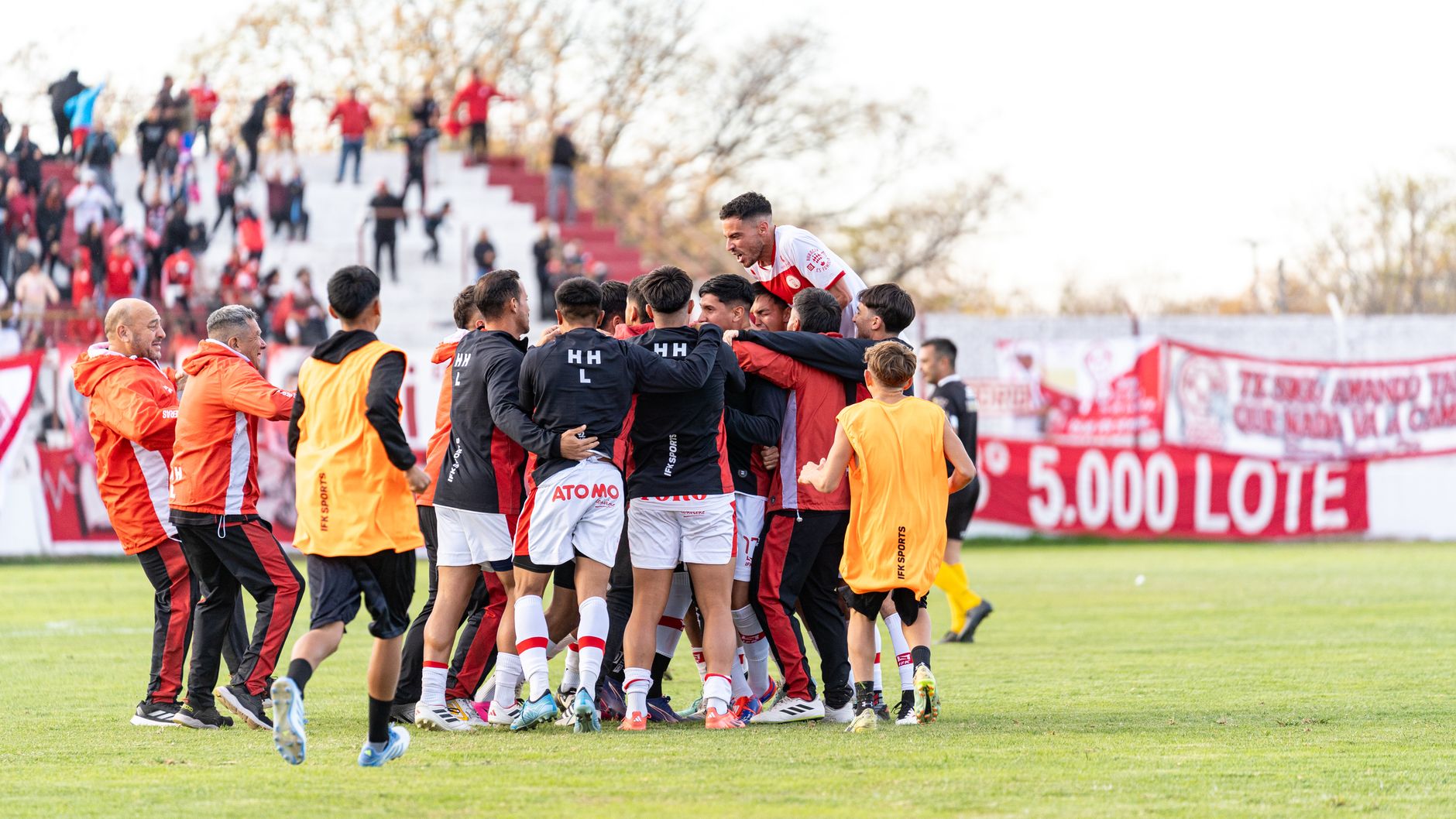 A team of joyful footballers celebrates a winning moment on the outdoor field.