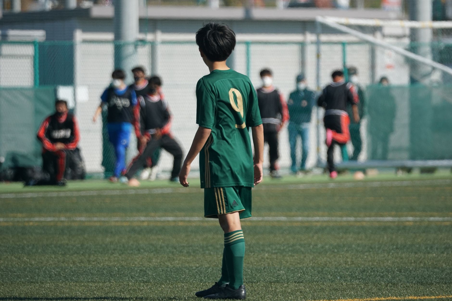 Youth soccer player in green jersey on football field during match.