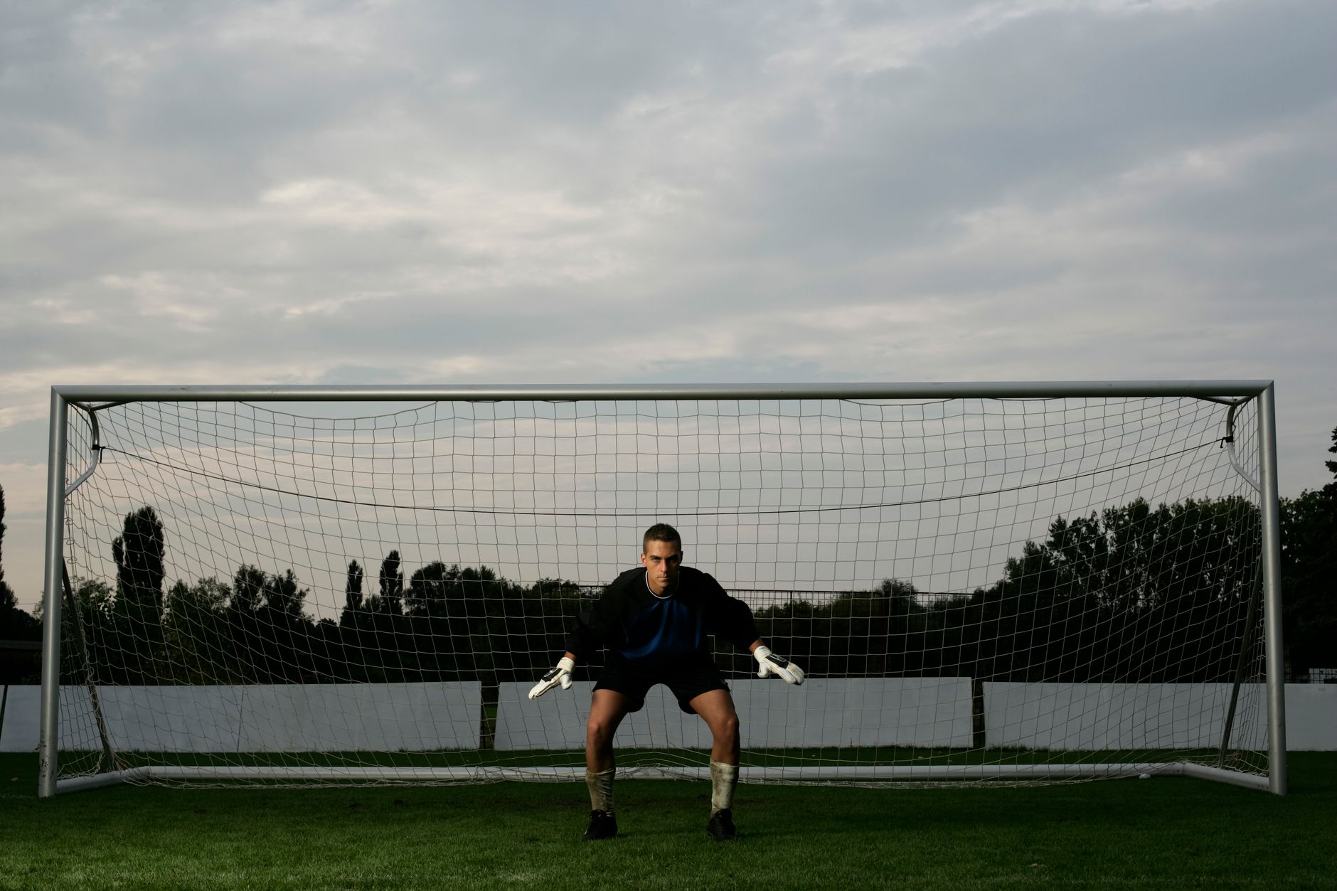 Soccer goalie in action stance ready for defense in front of the net at dusk.