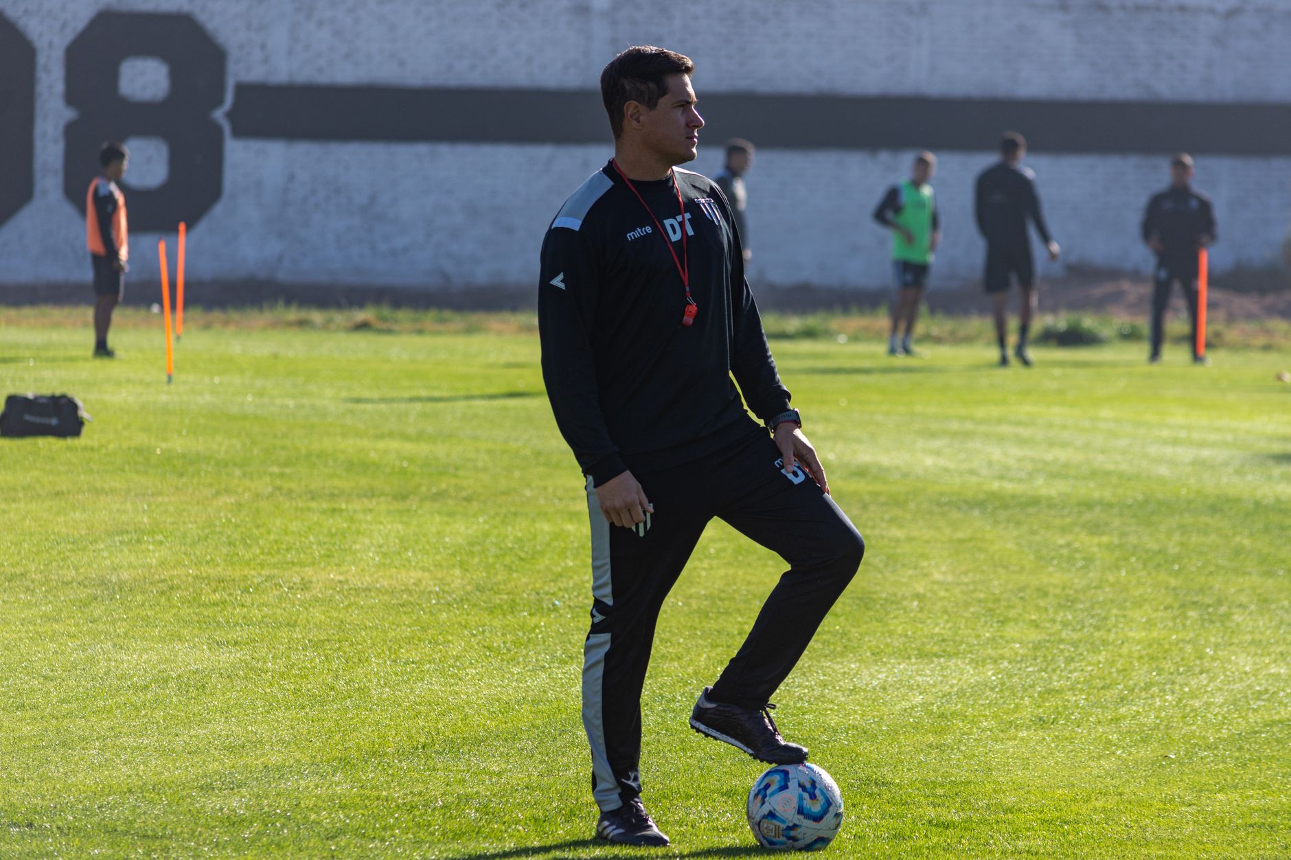 Adult soccer coach guiding players during outdoor training on a sunny day.