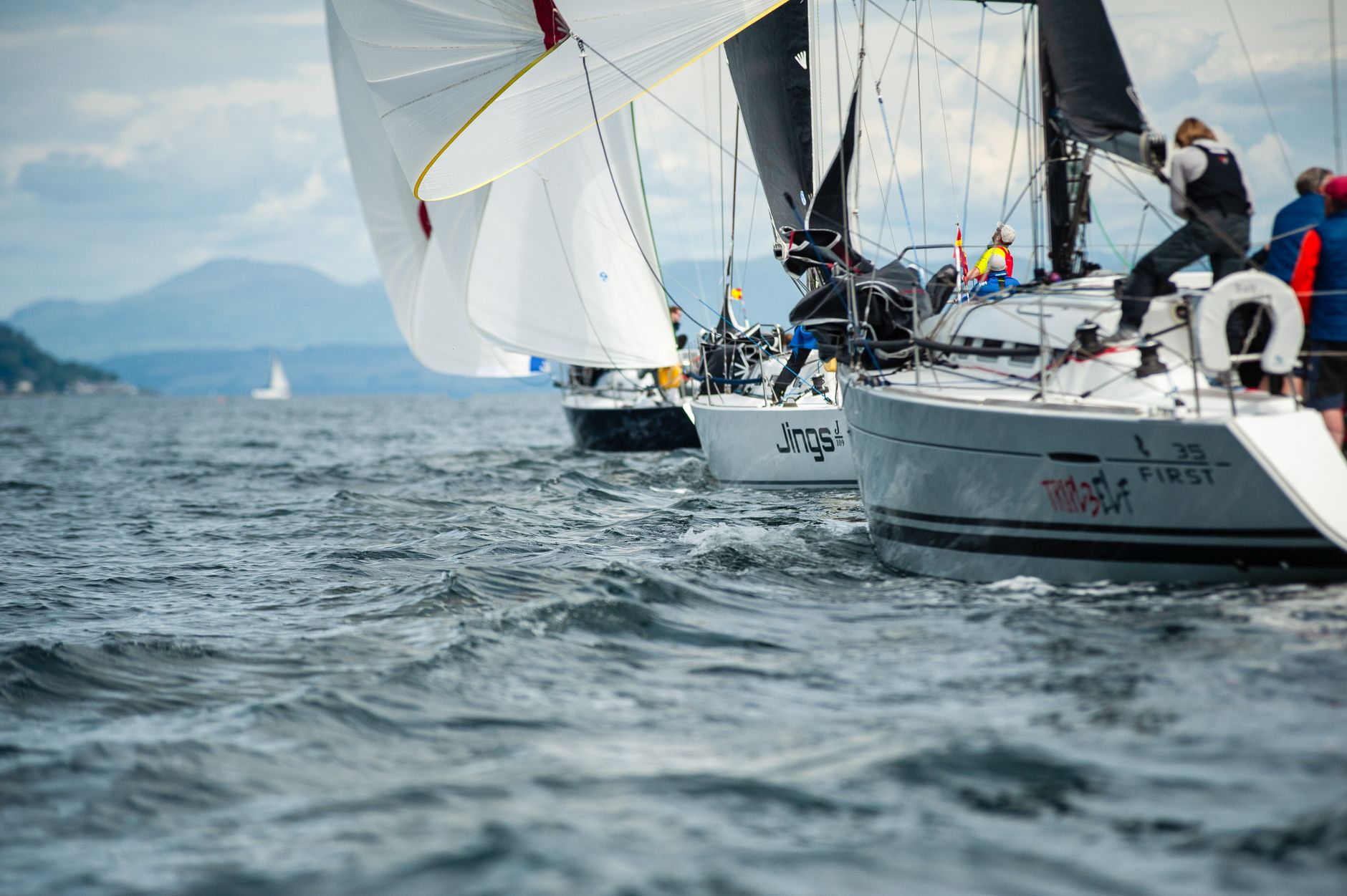 Sailboats racing in a thrilling regatta off the coast of Scotland with a backdrop of scenic hills.