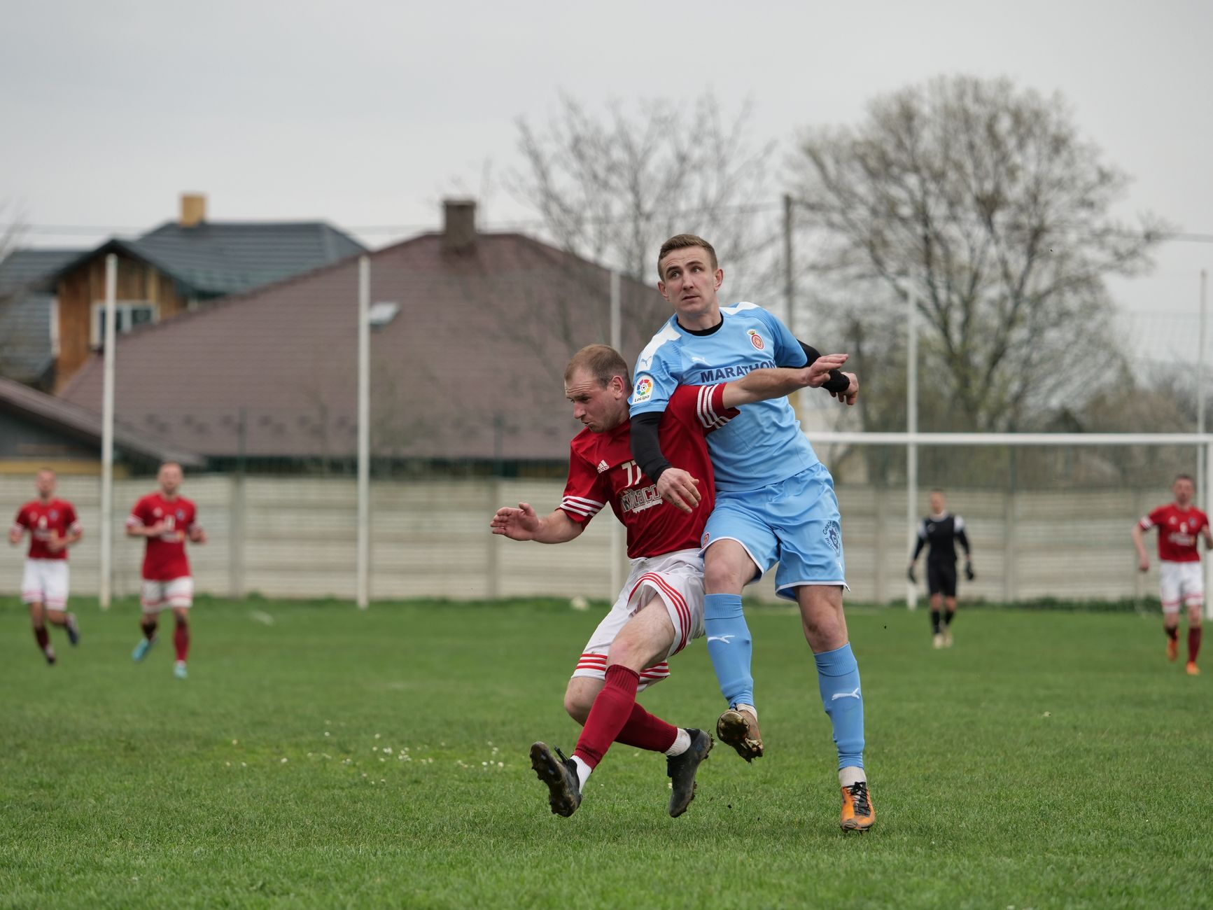 Players fiercely competing in a local football match on an outdoor grassy field.