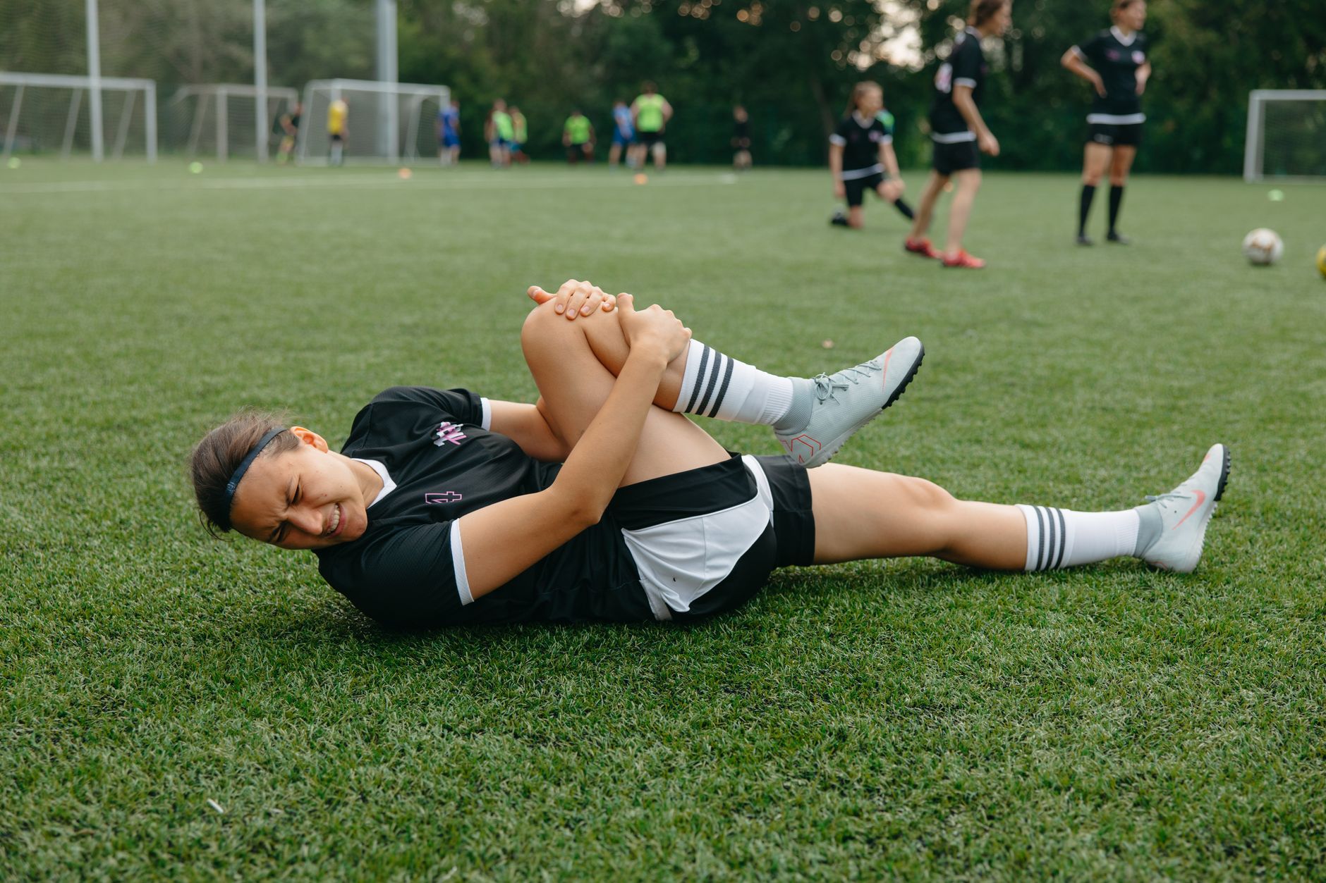 A female soccer player lying on the field, holding her injured leg in pain during a game.