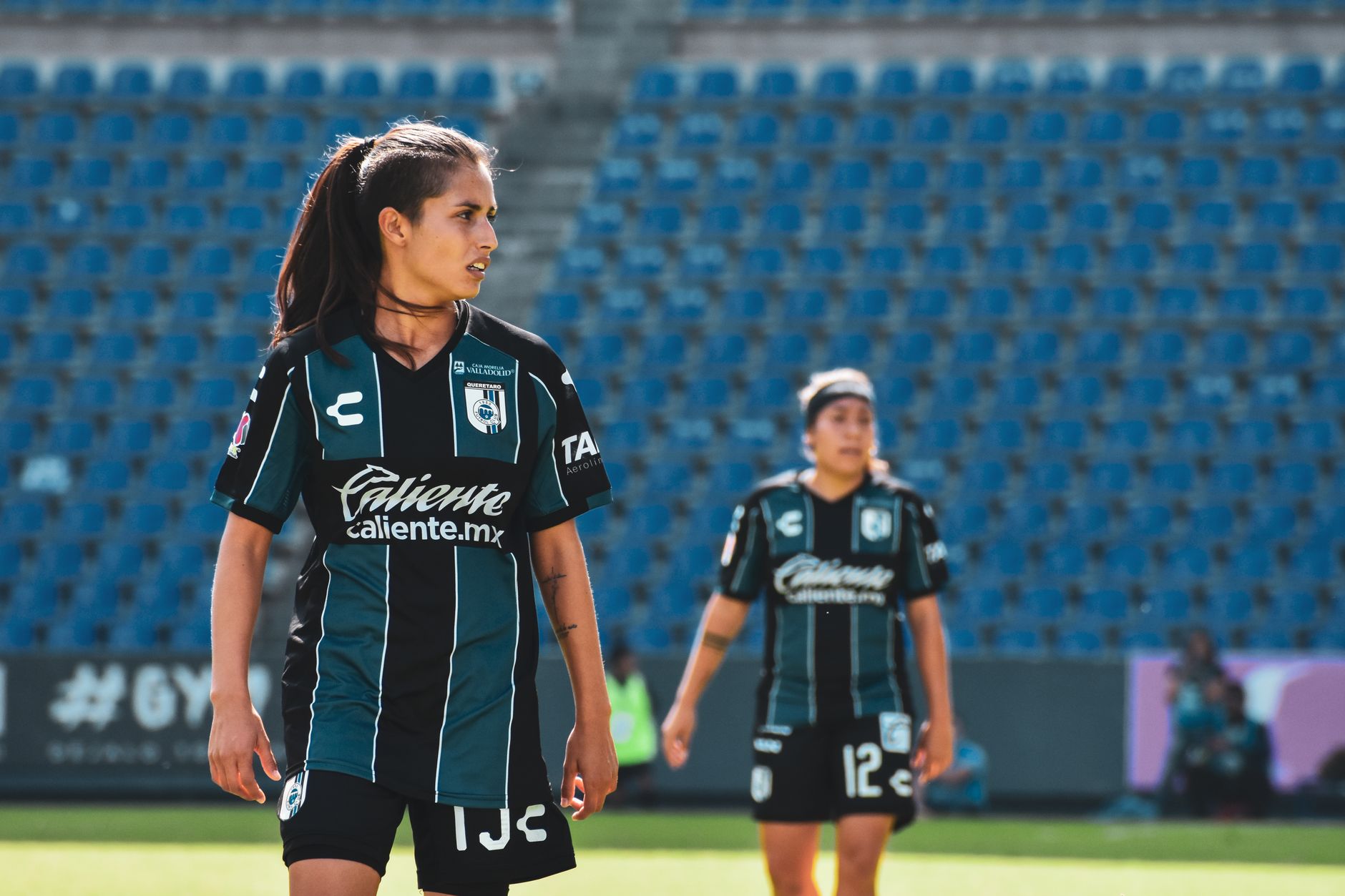 Female soccer players in action during a match at an outdoor stadium in Mexico.