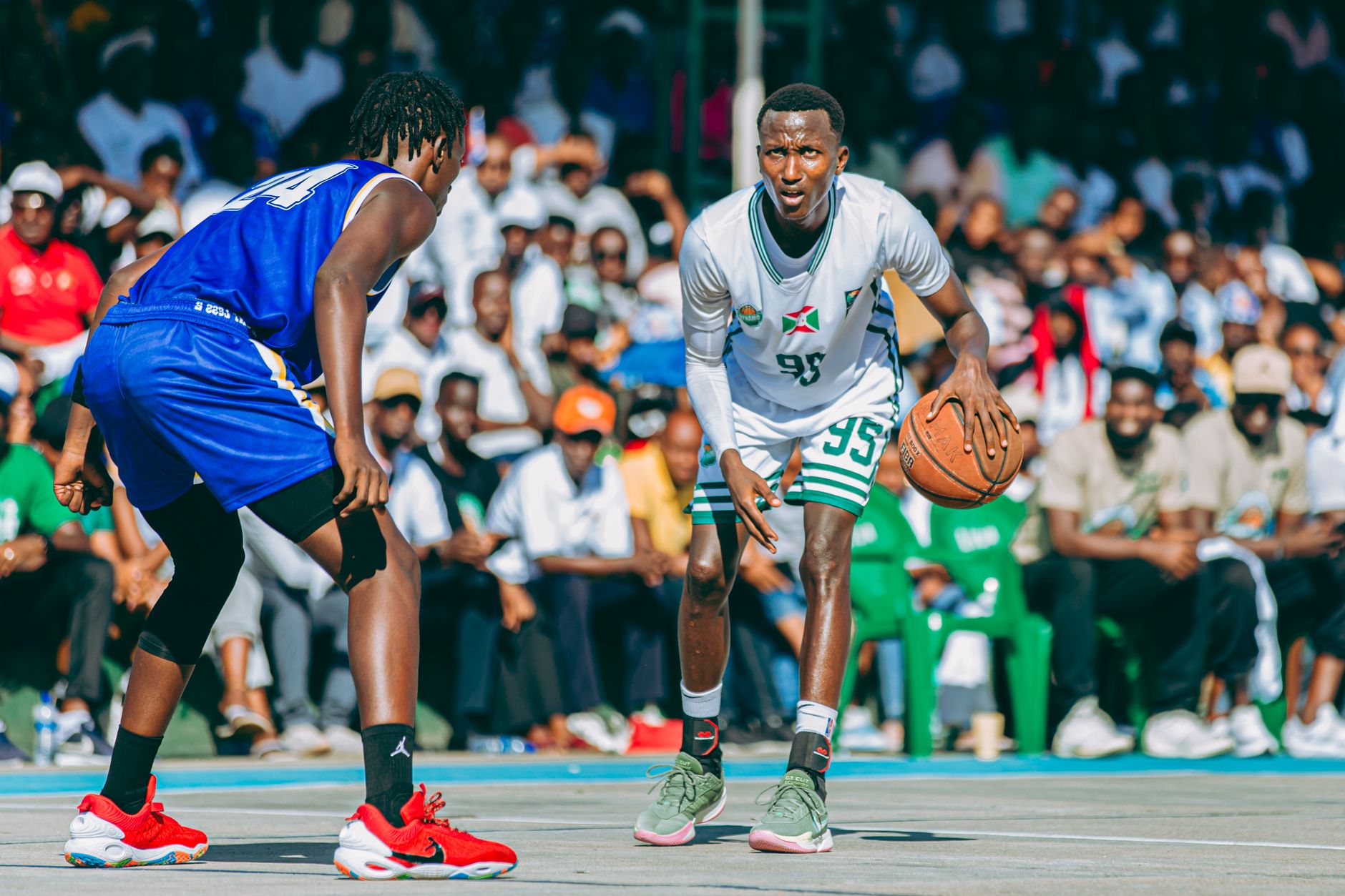 Intense outdoor basketball match with two players in focus, surrounded by a large audience.