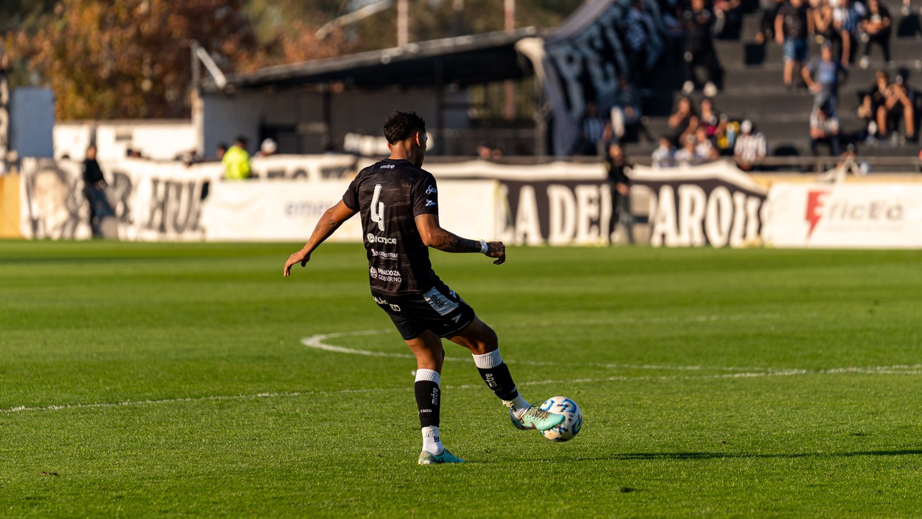 Soccer player wearing a black jersey kicking a ball on a grassy field during a match.