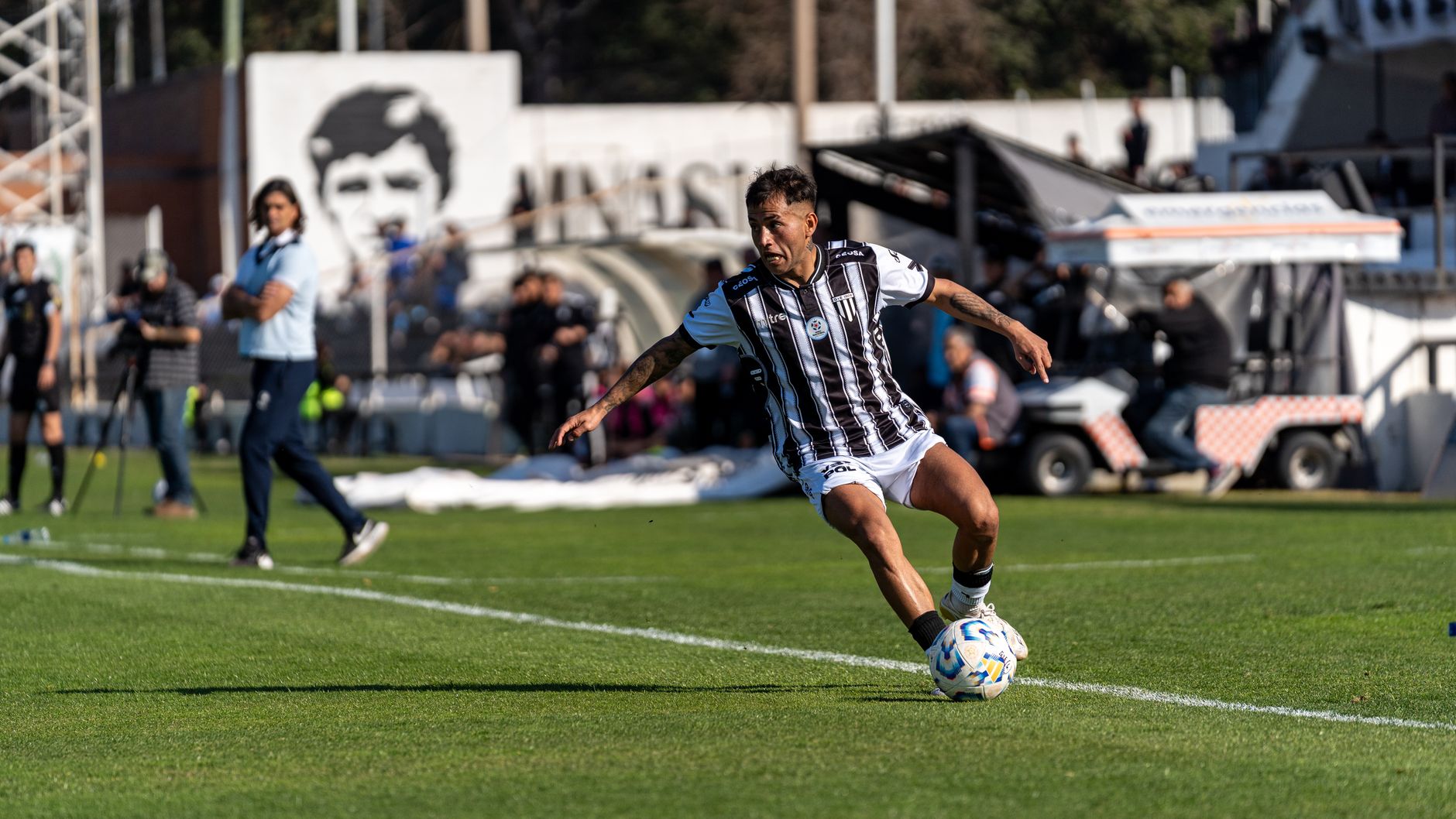 Dynamic shot of a footballer in action on the field during a sunny day match with spectators.