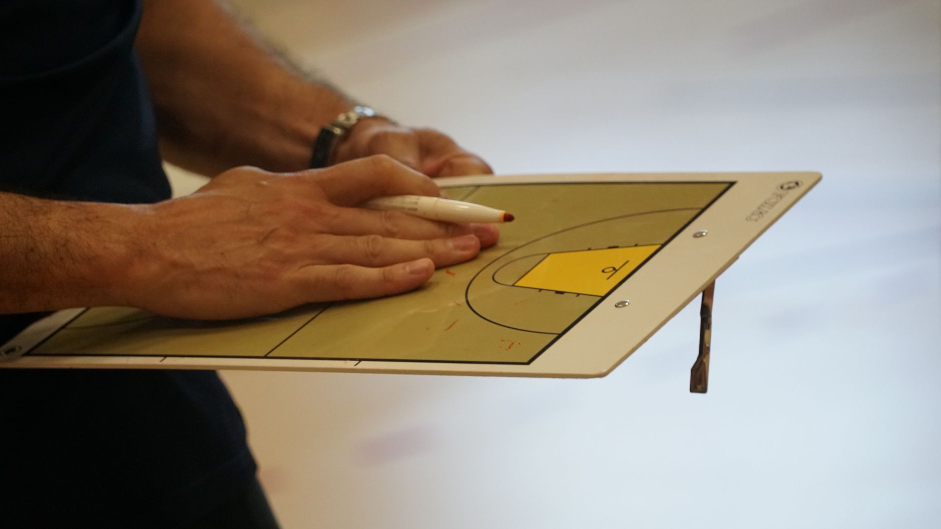 Close-up of a coach using a basketball tactics board to plan game strategy indoors.