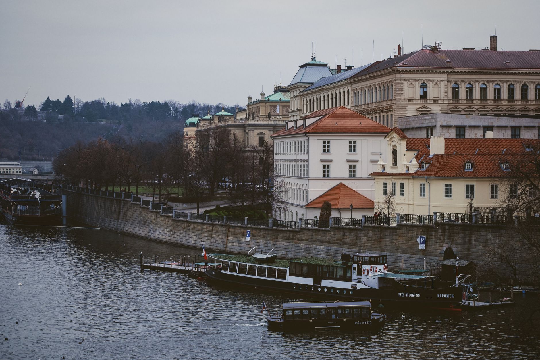 View of Prague's historic riverside with boats, classic architecture, and a tranquil river scene.