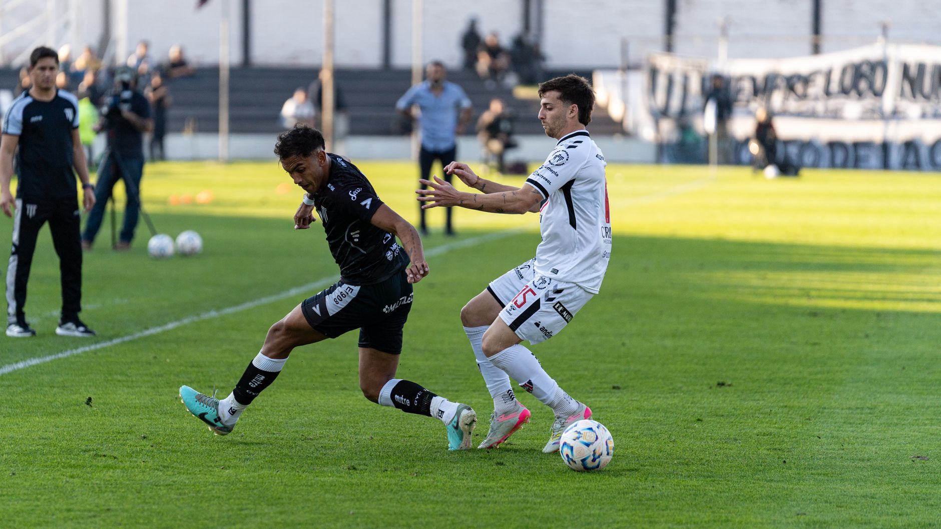 Intense action between two footballers competing in an outdoor match with clear daylight.