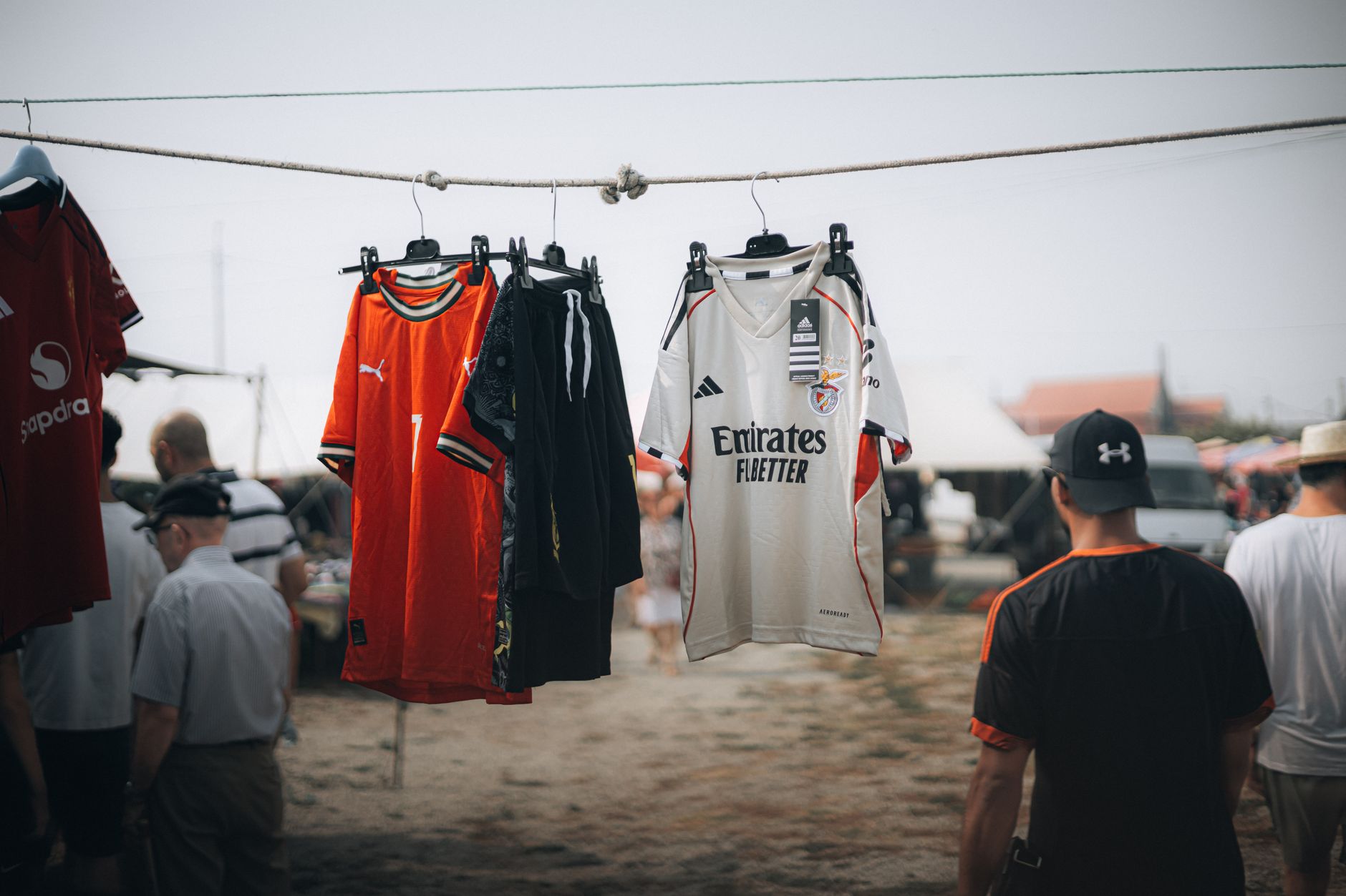 Colorful sports jerseys hanging at an outdoor market with people in the background.