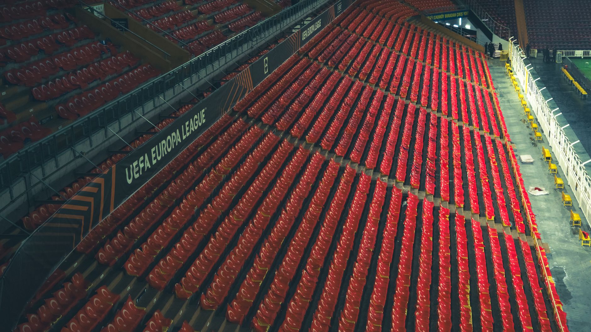 Rows of empty red seats in a UEFA Europa League stadium, captured from above.