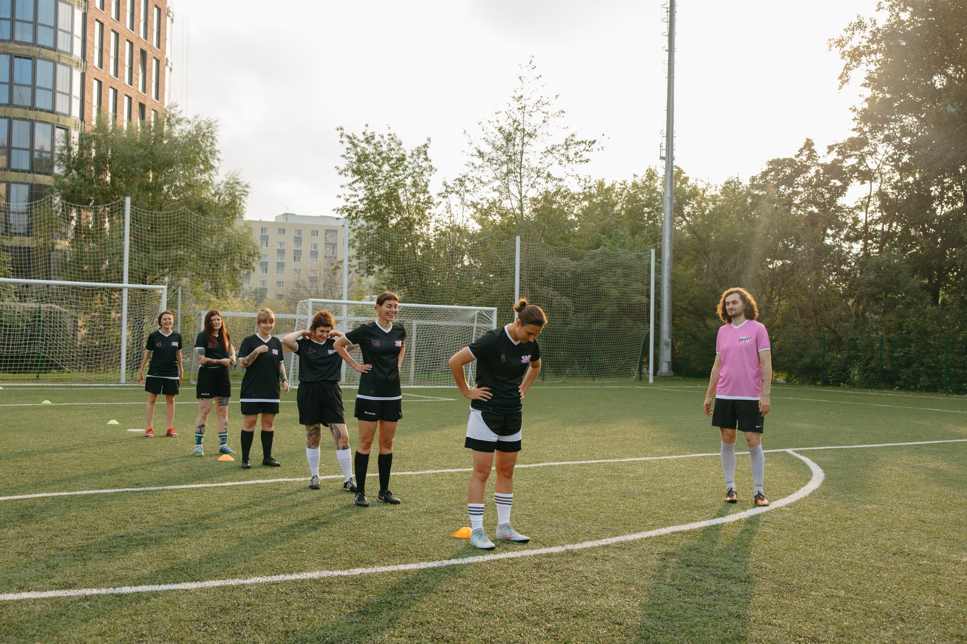 Women's soccer team practices drills on a sunny outdoor field with coach observing.