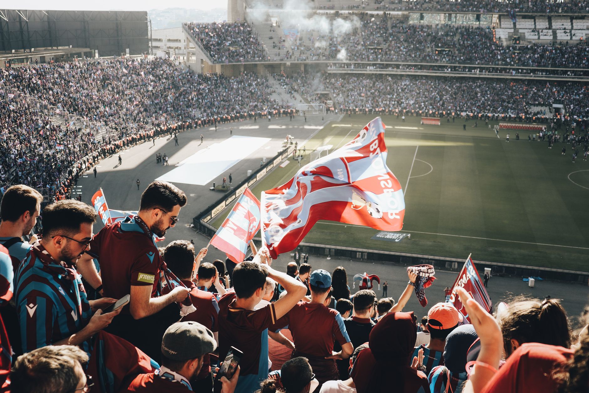 Vibrant crowd with flags cheering at a football stadium during the day.