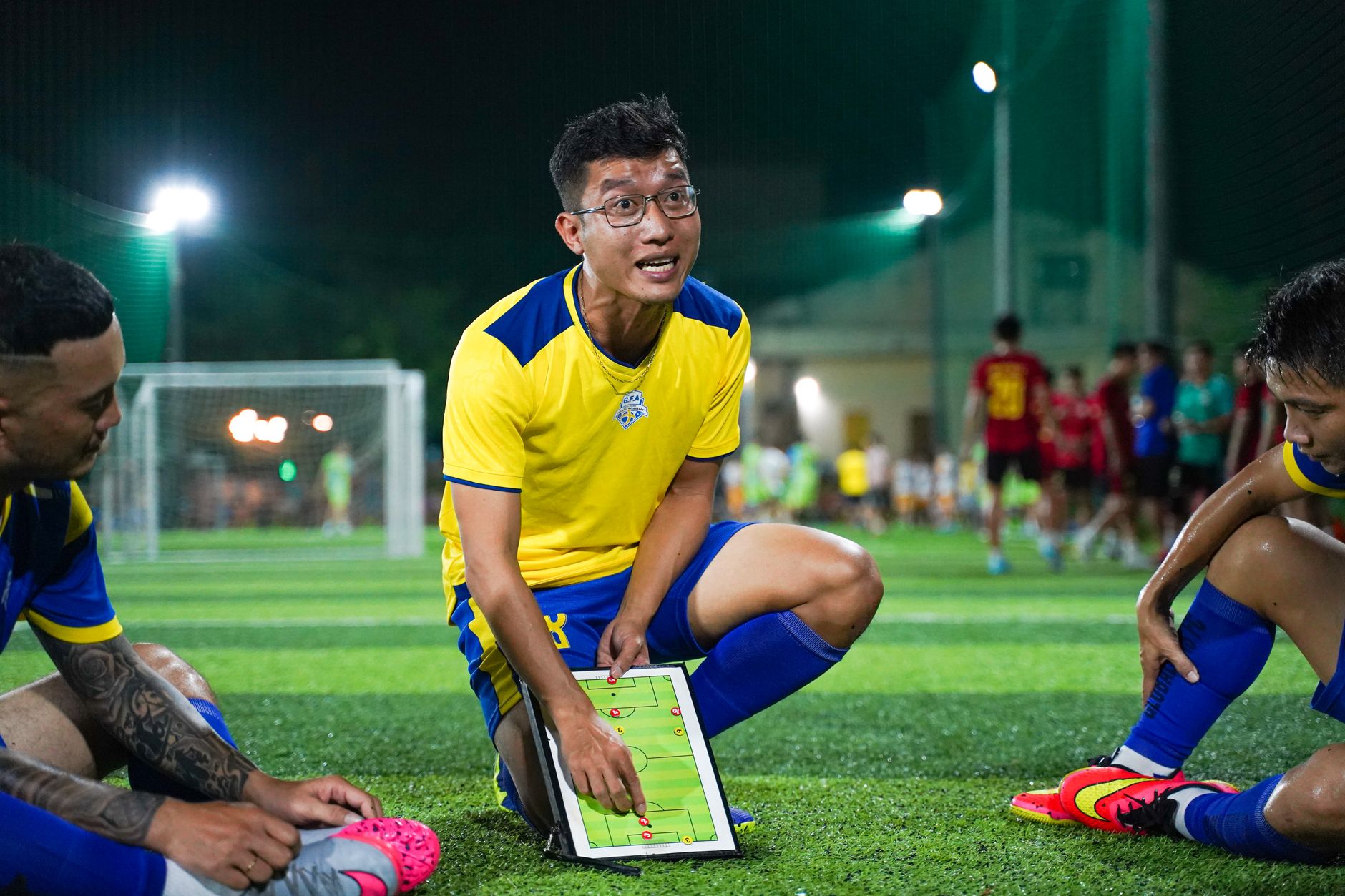 A soccer coach strategizing on a field with players during a night game session.
