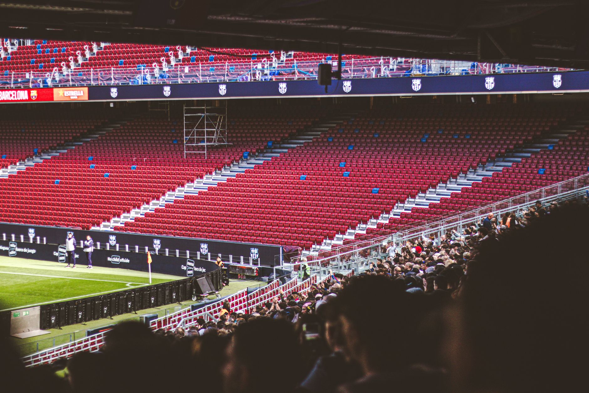 Panoramic view of stadium with empty red seats and crowd gathered for a live match.