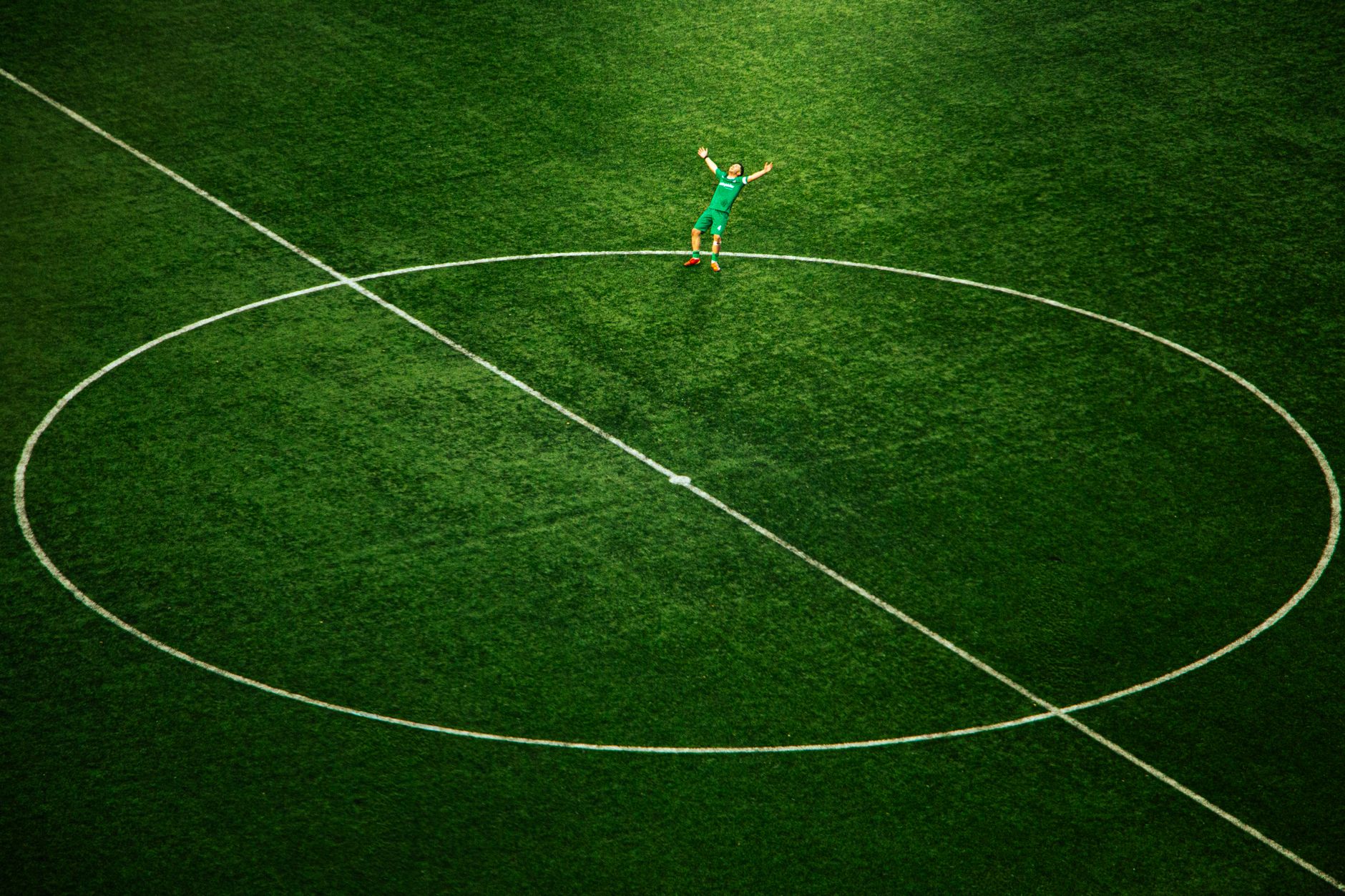 A soccer player celebrates on an empty field, spotlighted in the stadium's center circle.
