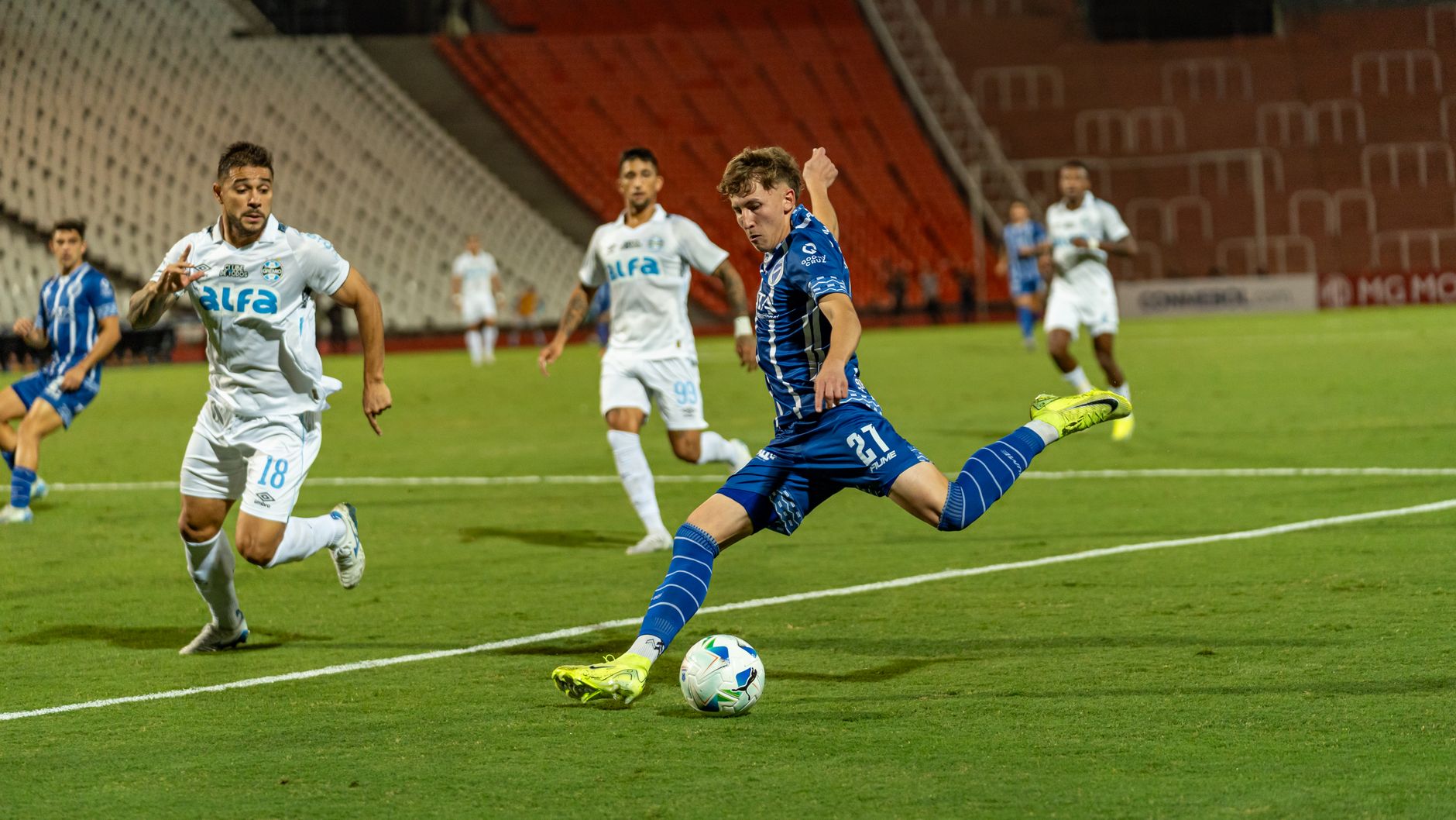 Dynamic action shot of a soccer match with players in blue and white jerseys on a green field.
