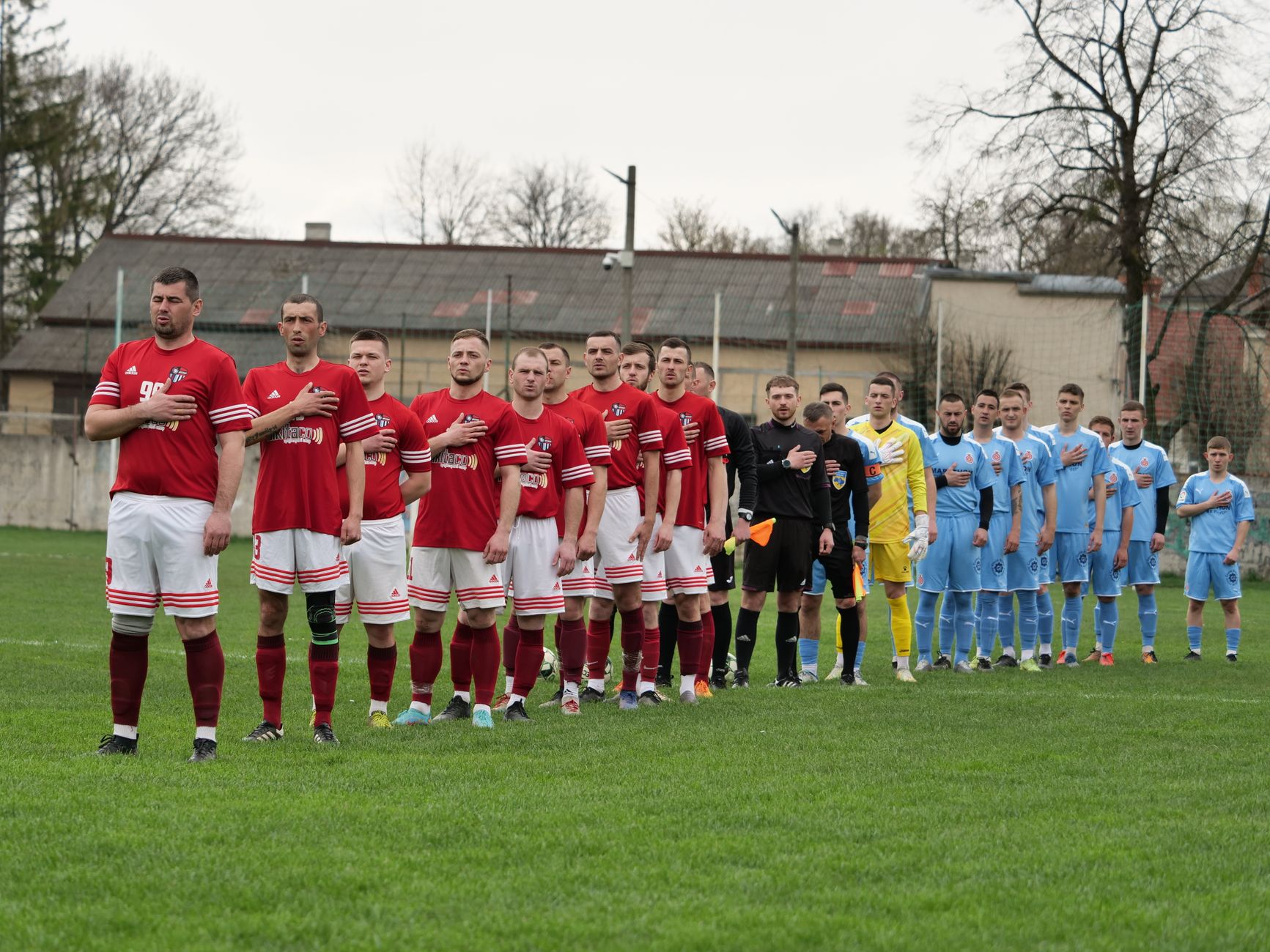 Two soccer teams stand in lines for a pre-match ceremony on a grass field.