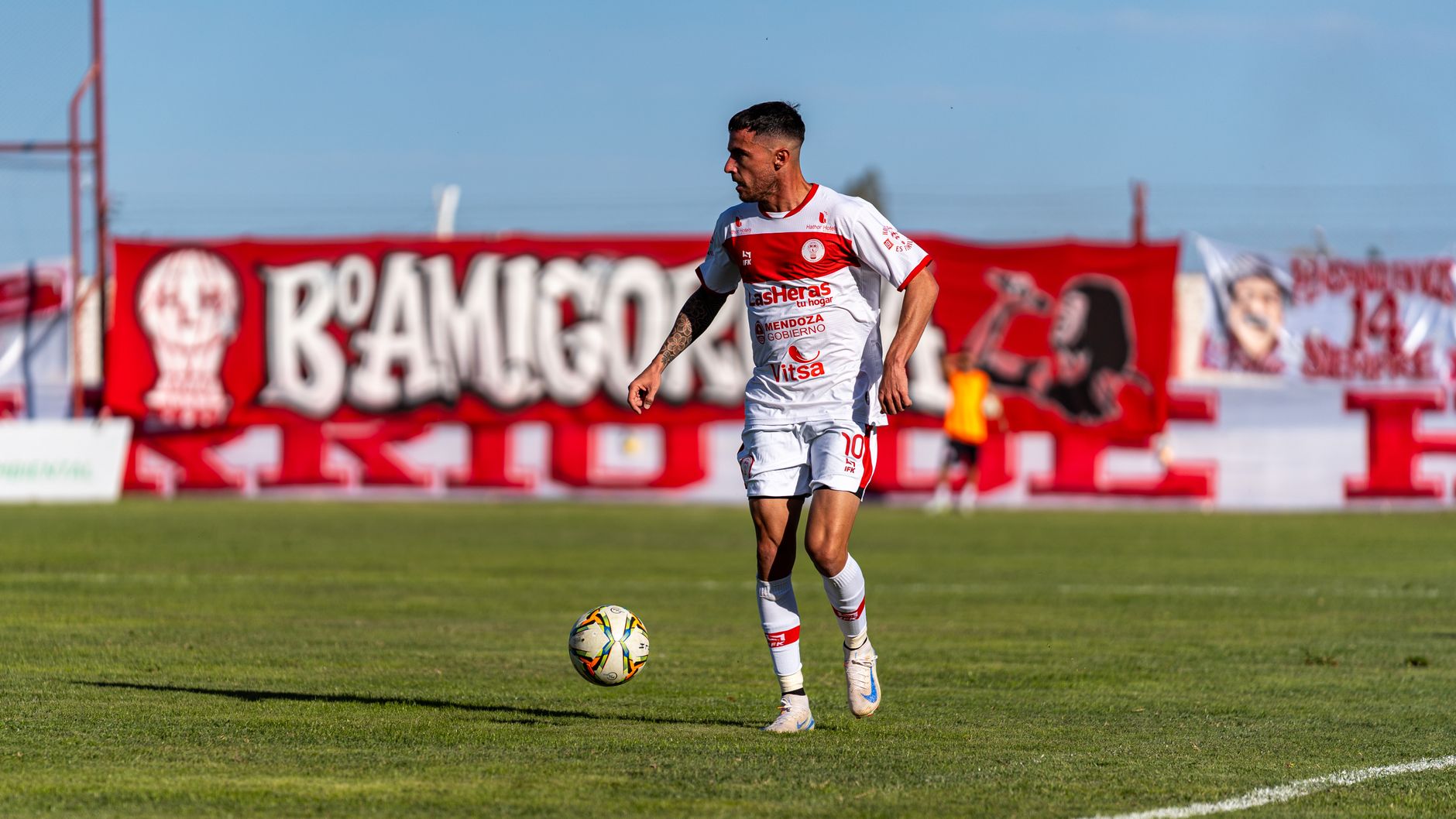 A football player in action on the field during a sunny day match with enthusiastic fans.