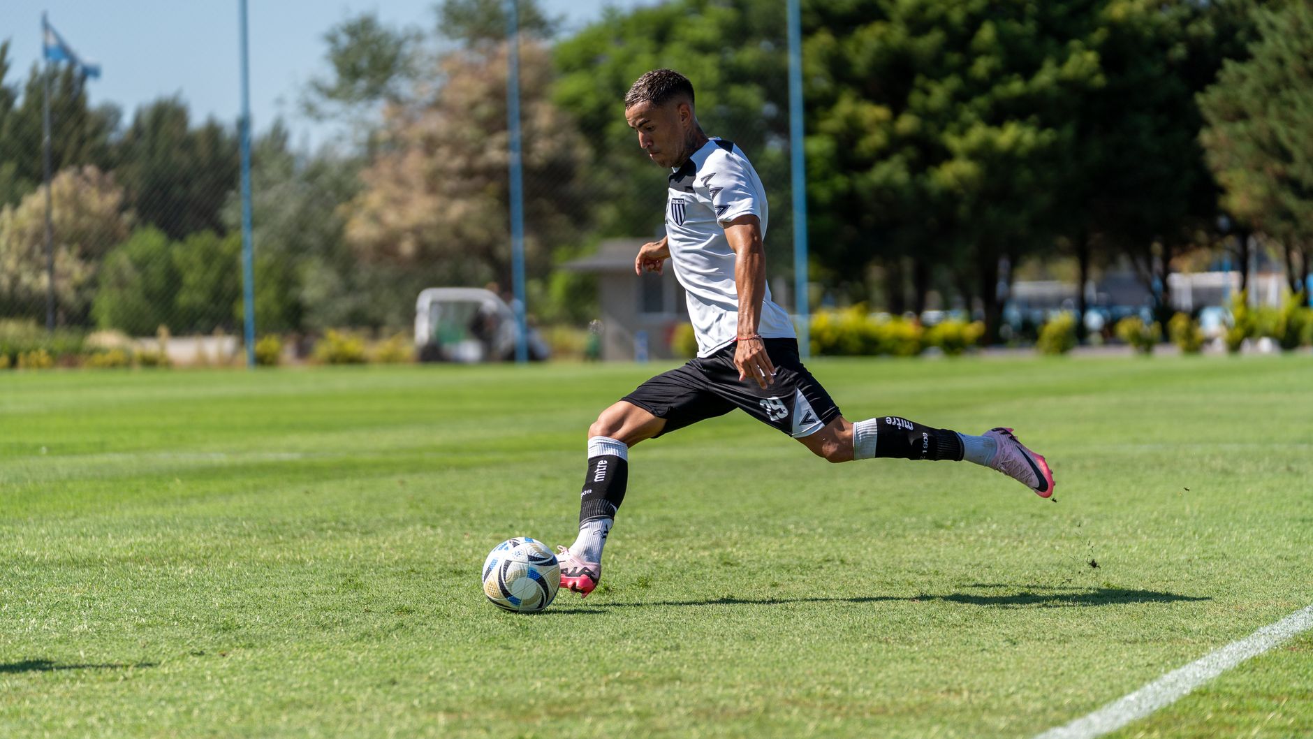 A soccer player in action kicking the ball on a sunny outdoor field during the day.