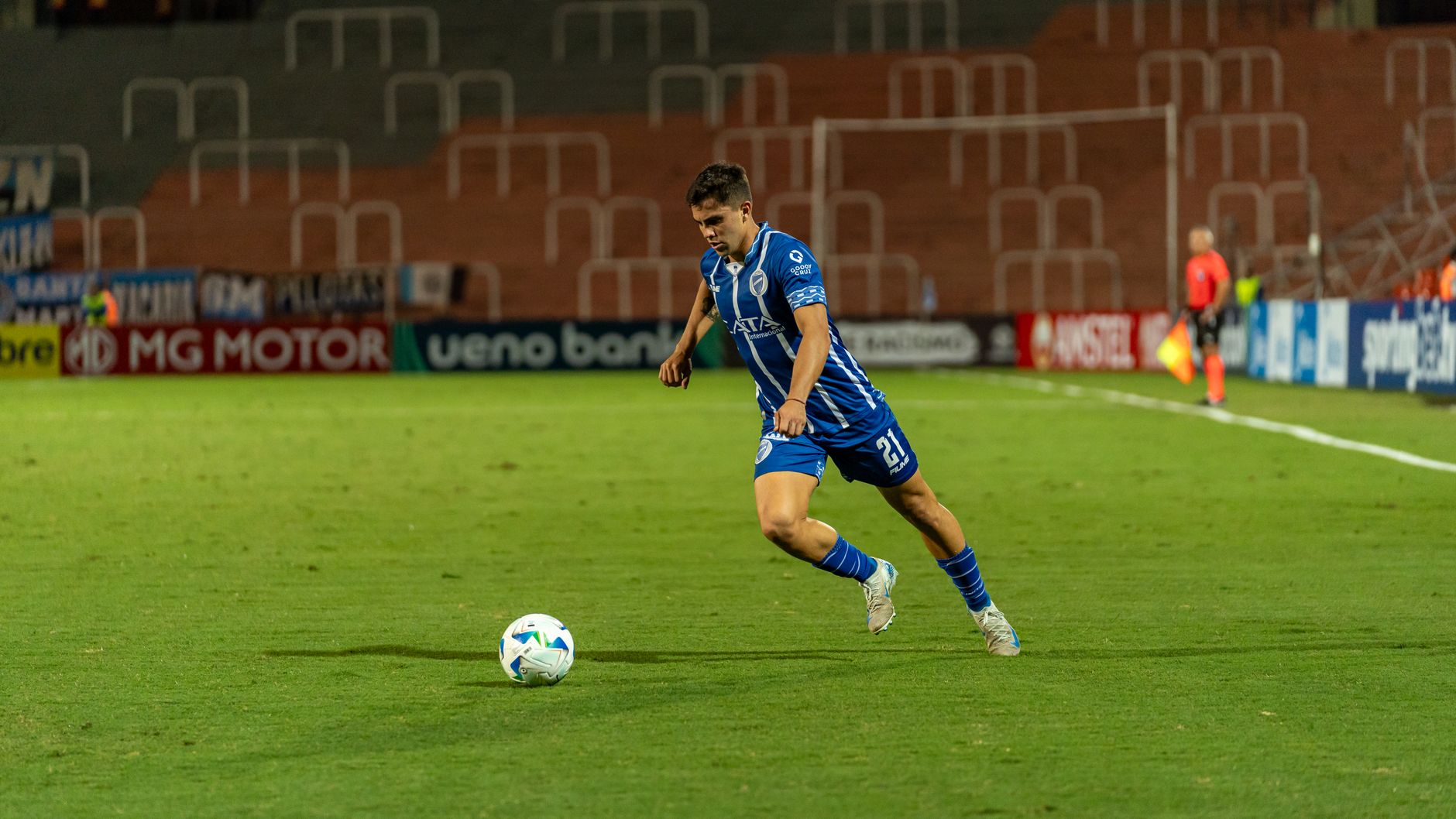 A soccer player in blue jersey dribbling the ball on a well-lit field during a night match.
