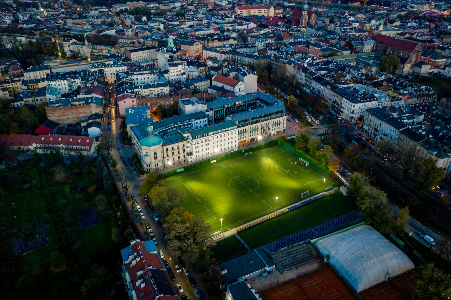 Aerial photograph showcasing a lit soccer field amidst an urban Polish cityscape during twilight.