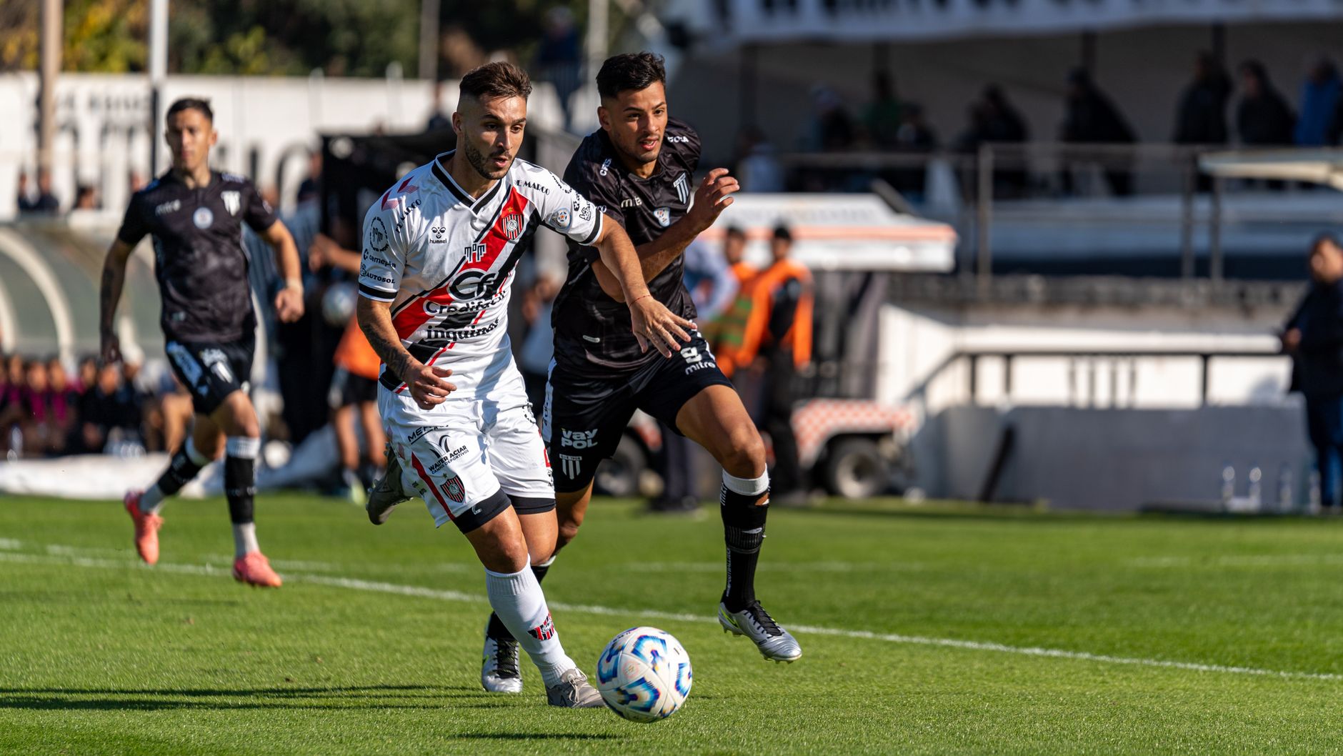 Two soccer players fiercely competing for the ball during a thrilling outdoor match on a sunny day.