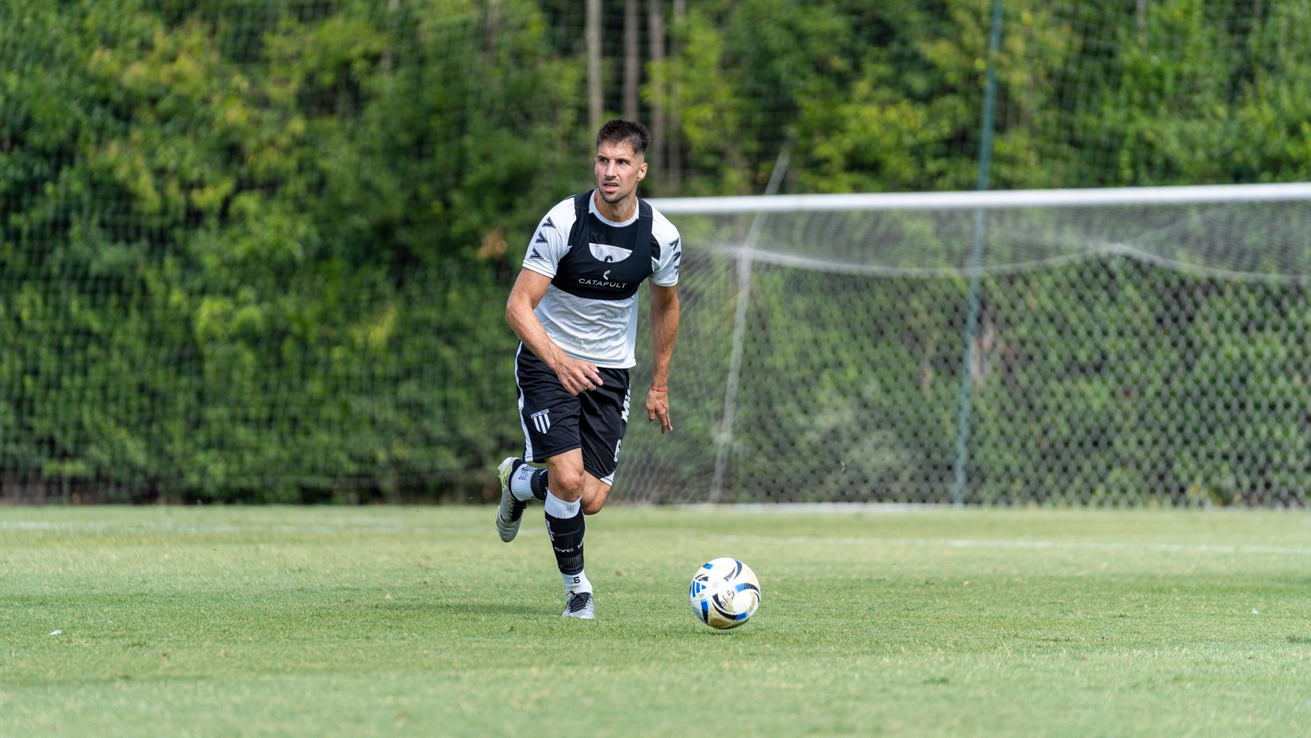 Soccer player running with the ball on a grassy field during a daytime practice.