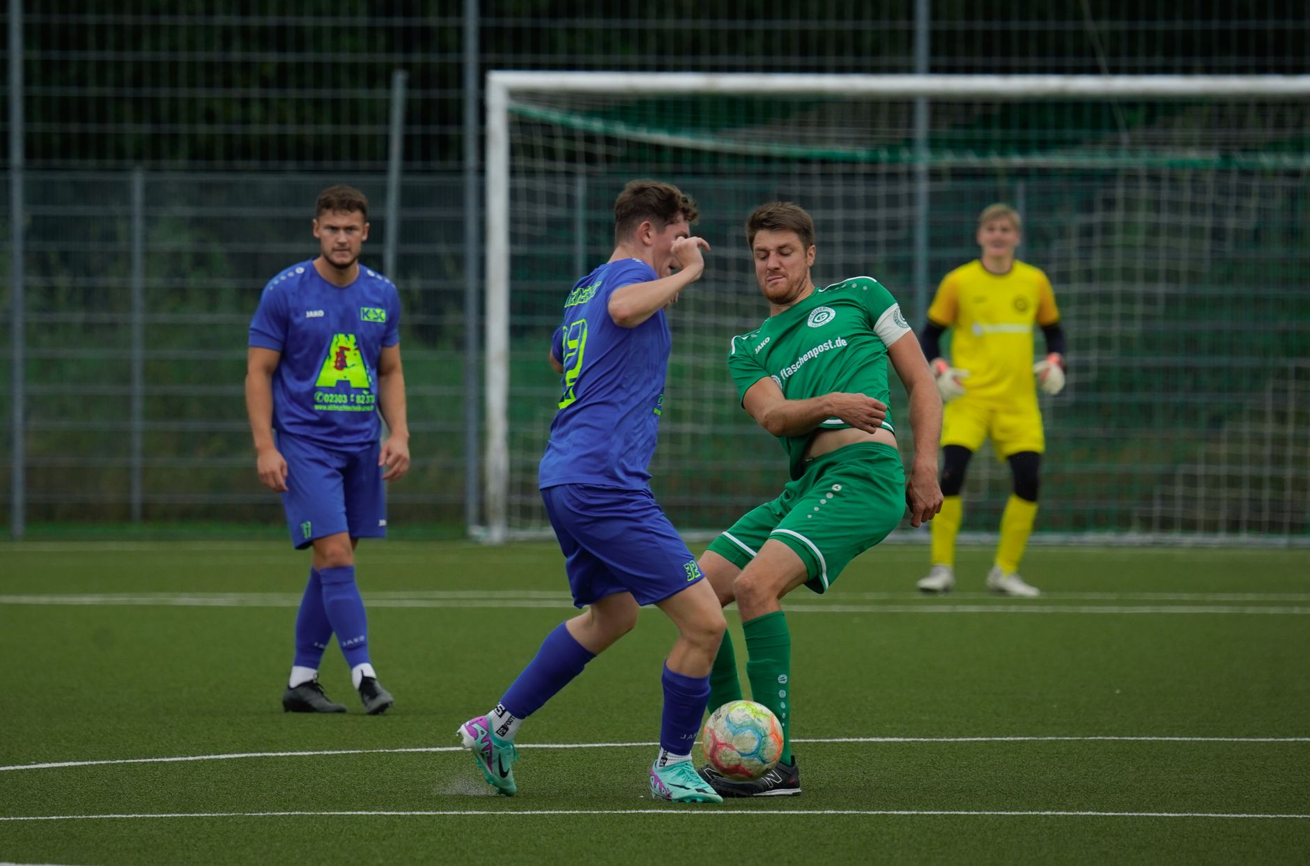 Soccer players in action during a competitive match on a green football pitch.