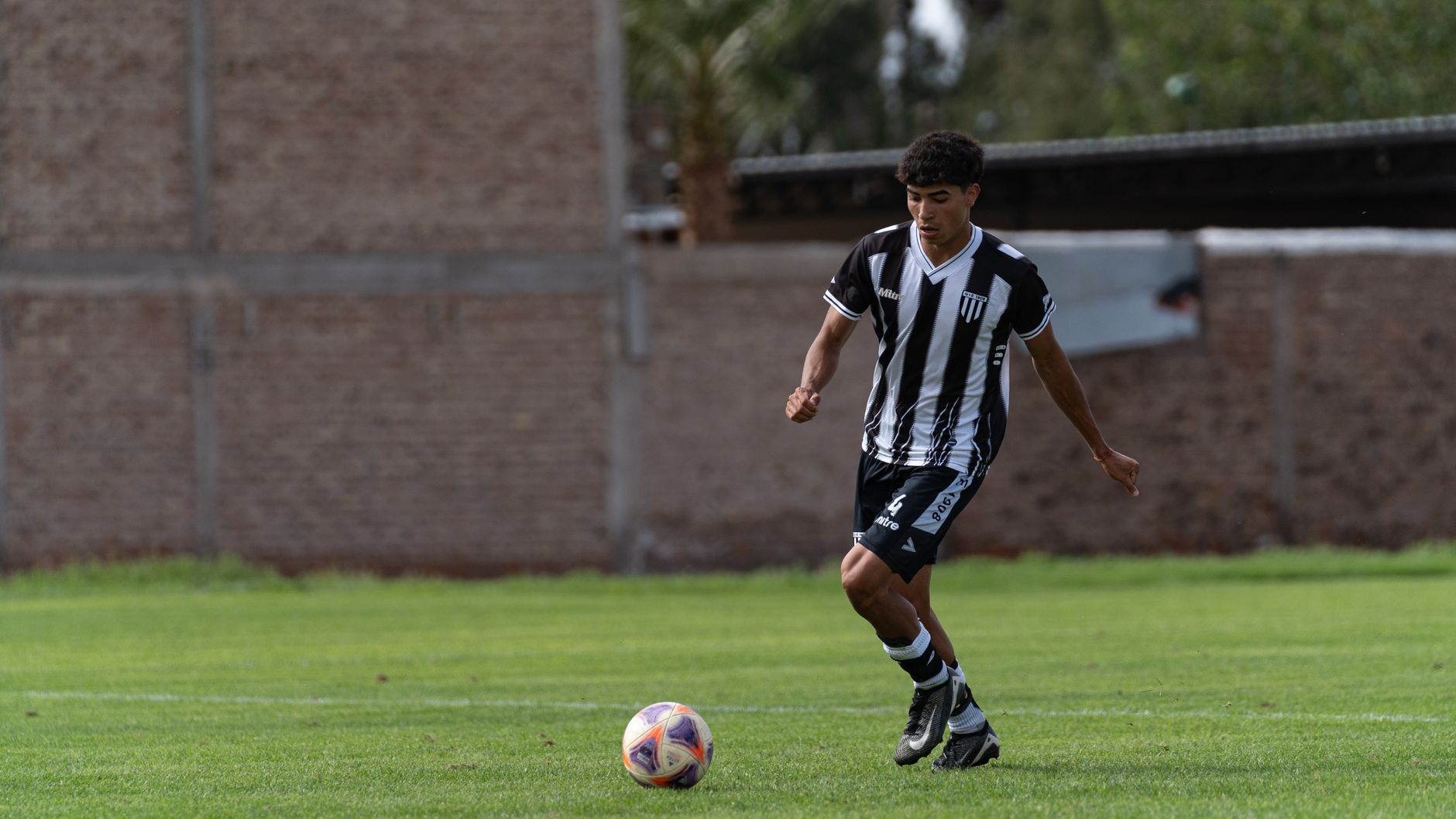 Young male soccer player dribbling on an outdoor field.