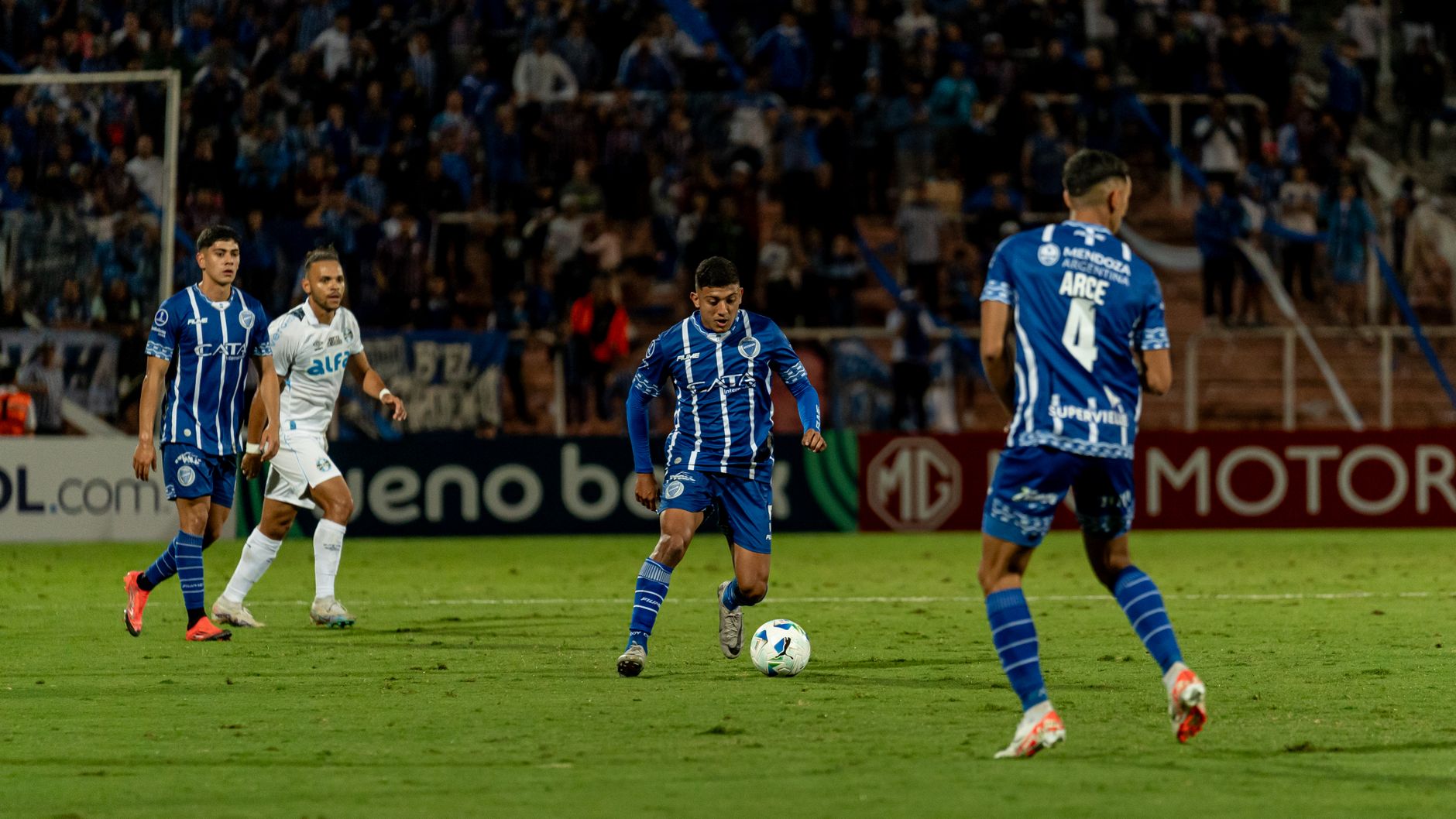 Players in action during an exciting night football match with vibrant crowd energy.