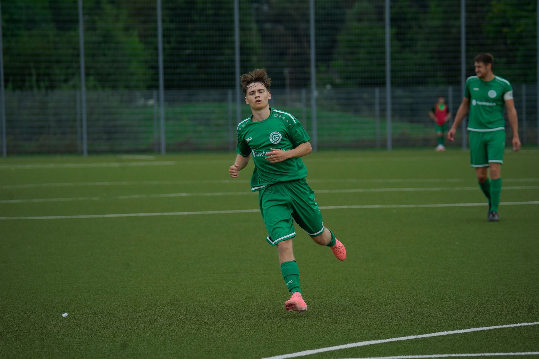 A football player in a green jersey running during an outdoor match on a grass pitch.