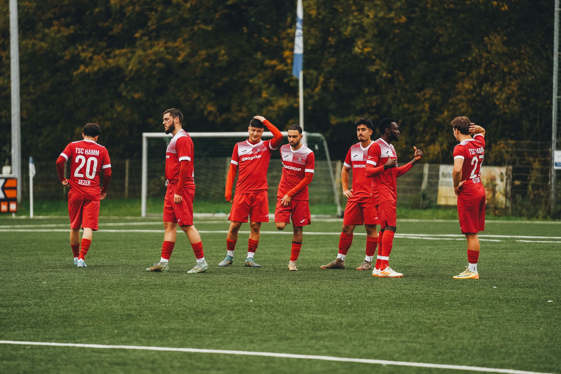 Amateur soccer team in red uniforms gathering on a green field during daytime.