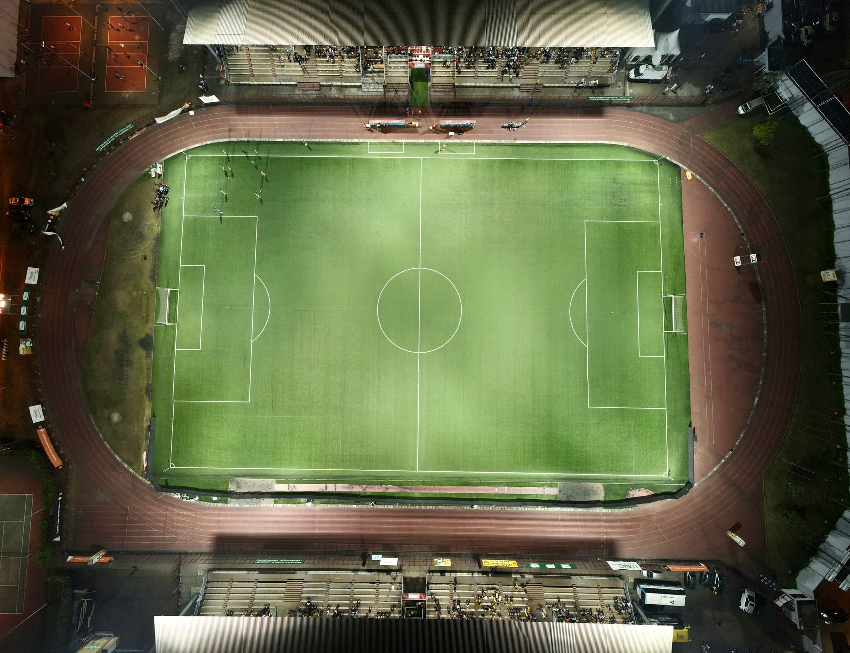 Top-down aerial view of a football stadium illuminated at night with minimal crowd.