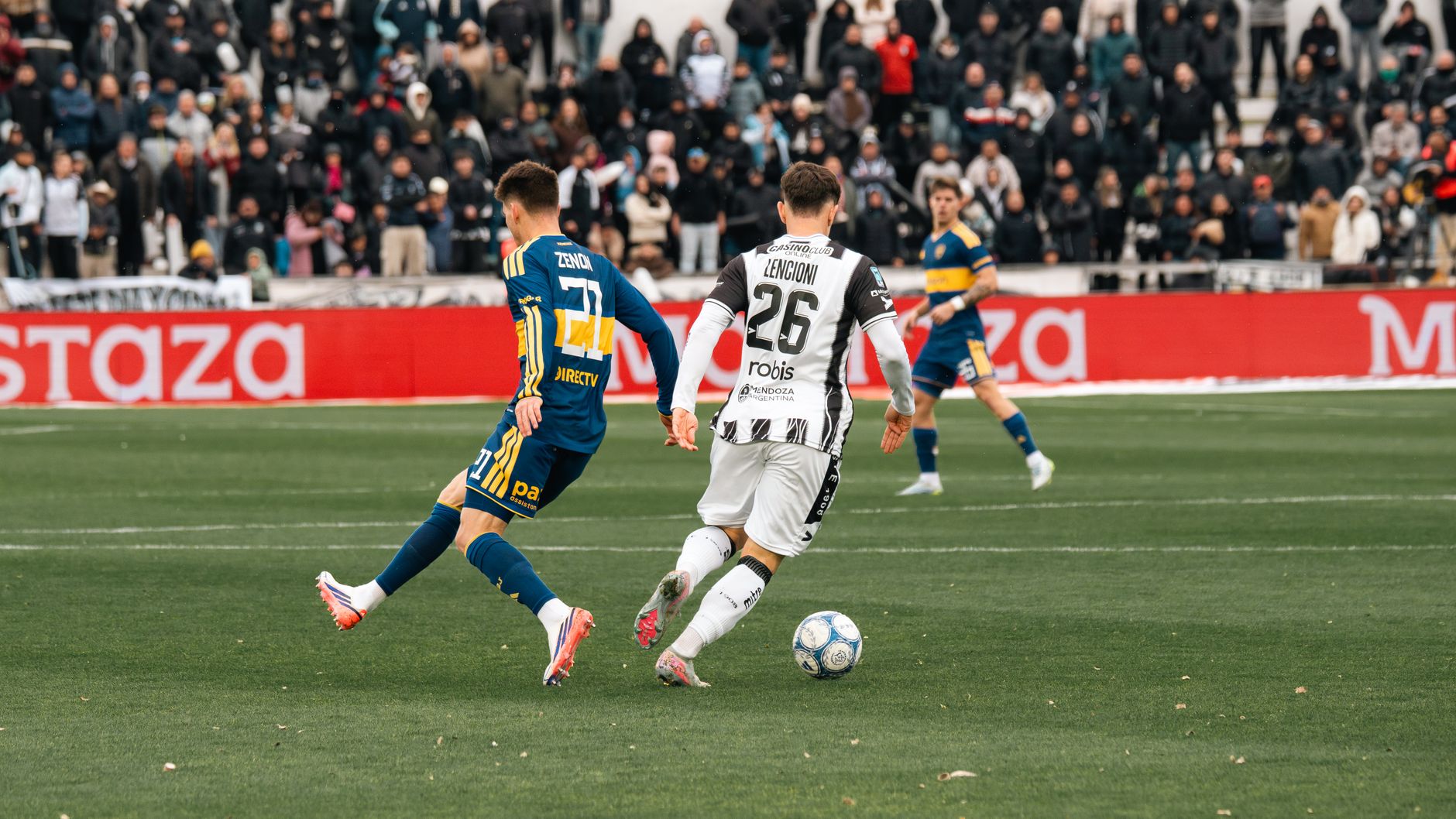 Soccer players in action during a competitive match with a full stadium of spectators.