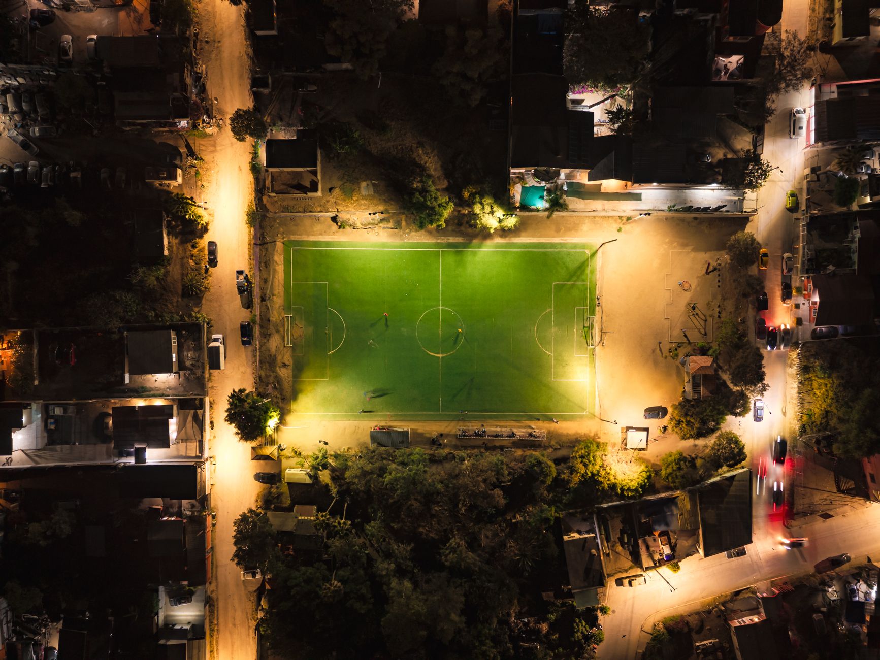 Aerial image of a brightly lit soccer field surrounded by urban lights at night.